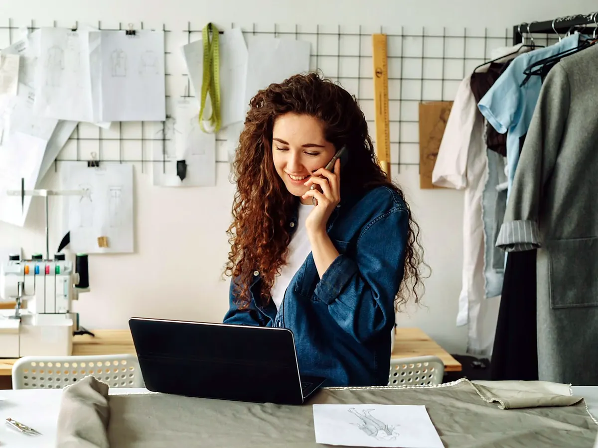 Dona de ateliê de costura falando ao telefone no seu espaço de trabalho