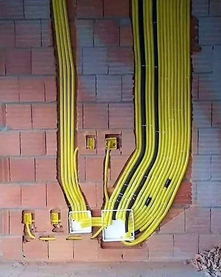 Fiação nova passando por eletrodutos amarelos em parede de obra, antes do reboco