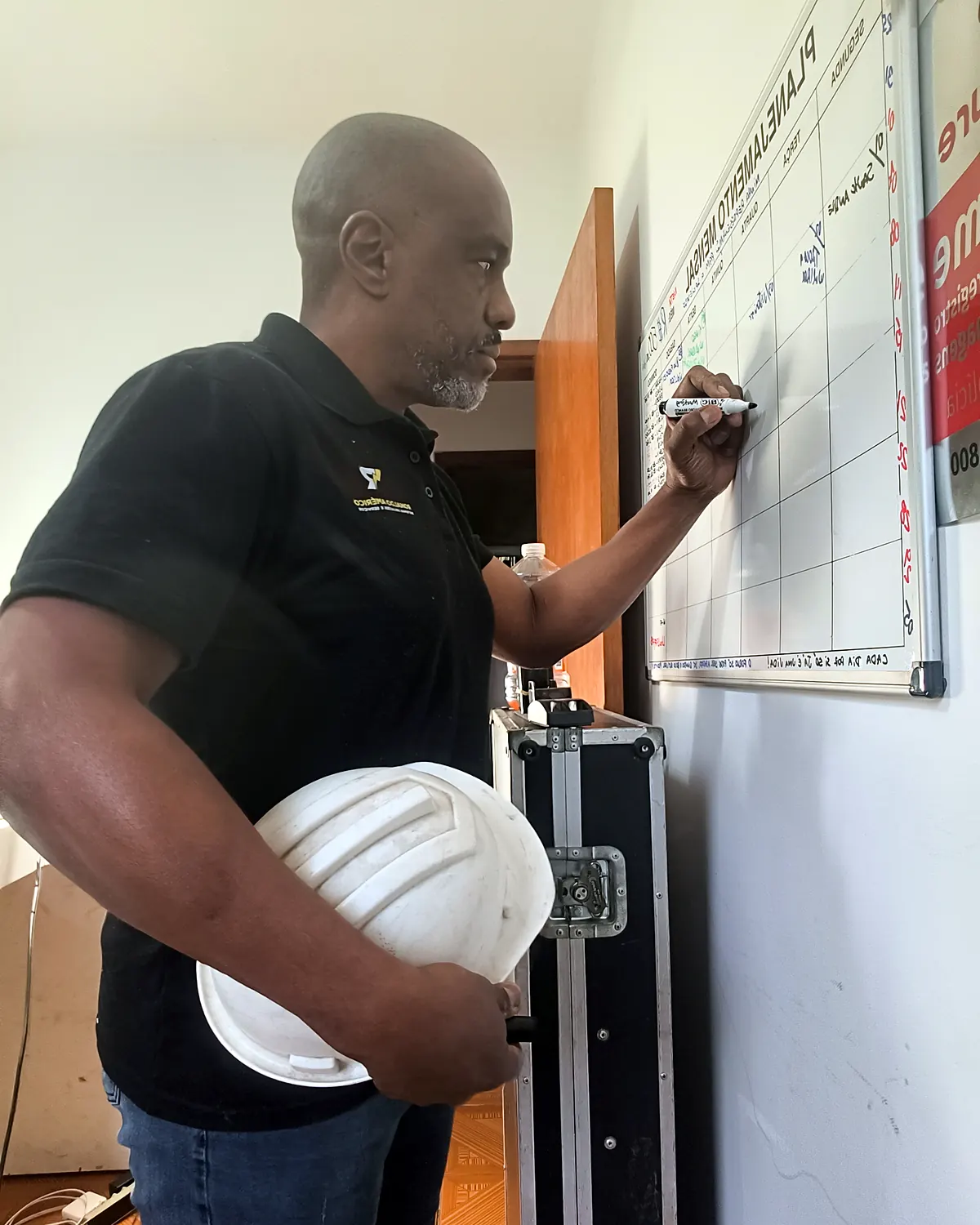 Ronaldo Américo planejando serviço elétrico no quadro branco, com capacete de segurança