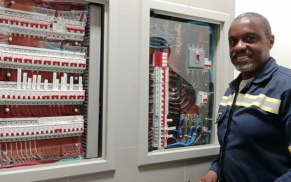 Eletricista Ronaldo Américo ao lado de quadros de distribuição organizados conforme a NBR 5410